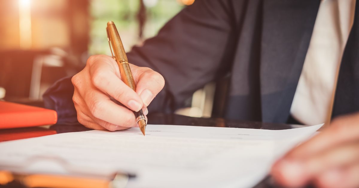 Close up of a professional business man, writing with a gold pen on his legal paperwork.