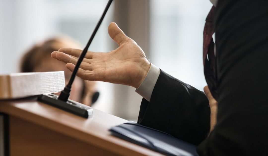 Close up of a lawyers hands as he gestures from behind the podium in court.