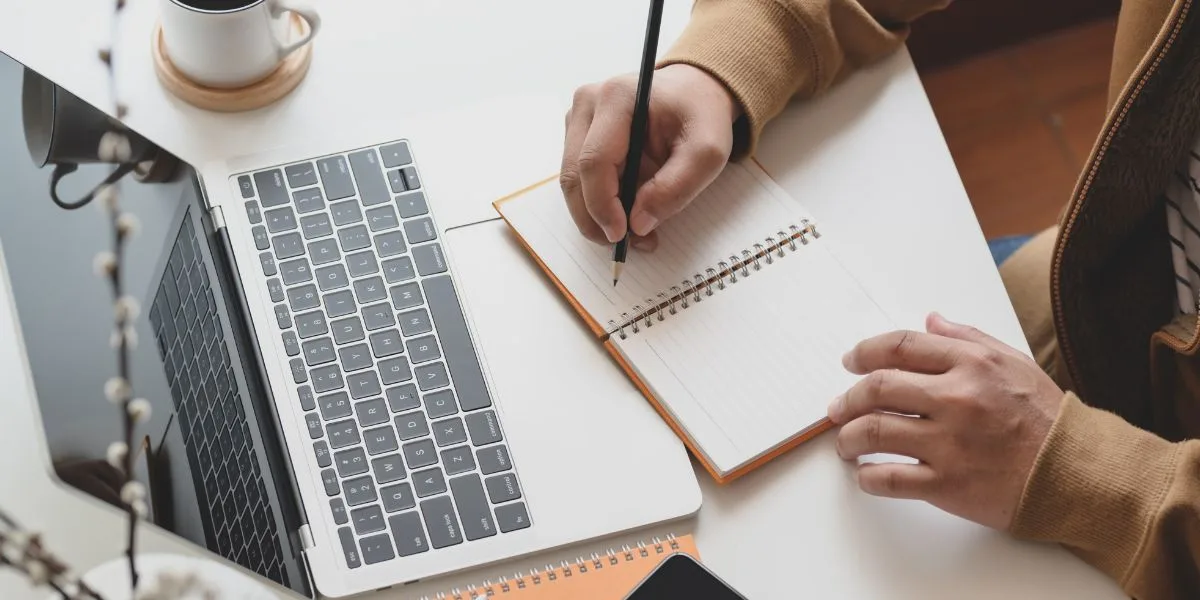 Professional takes notes on their notepad as they sit in front of a computer, ready to participate in a webinar