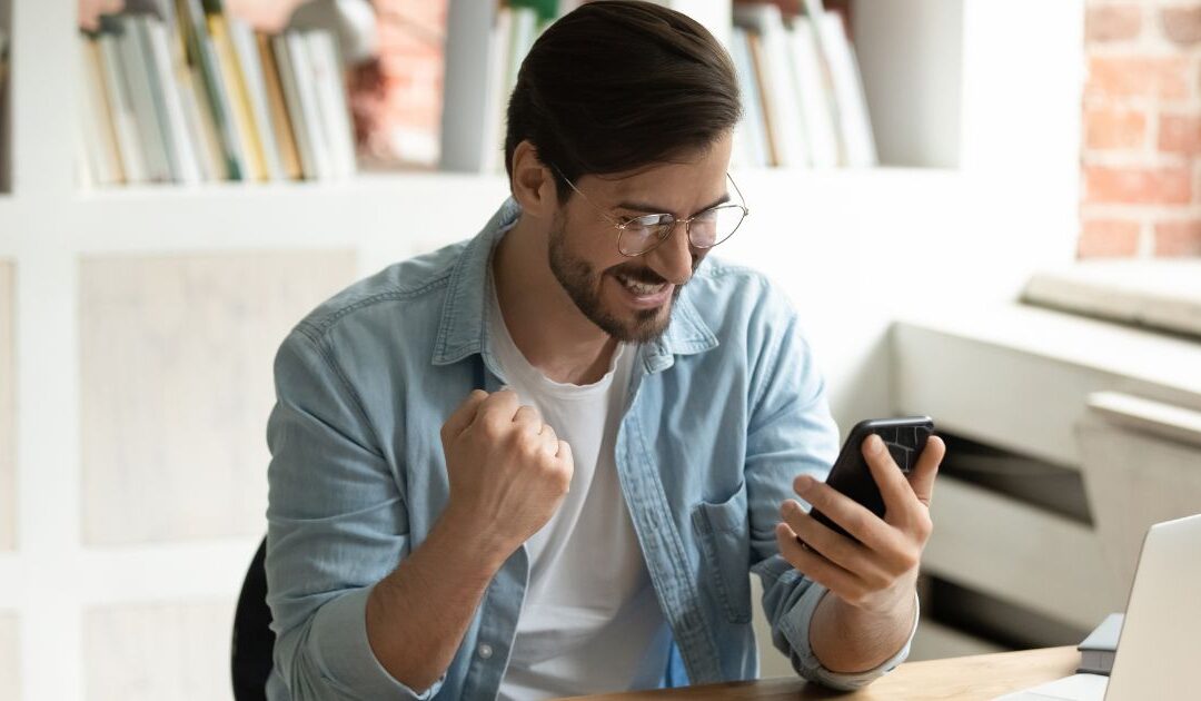 Professional man at his desk celebrates good news he sees on his cell phone