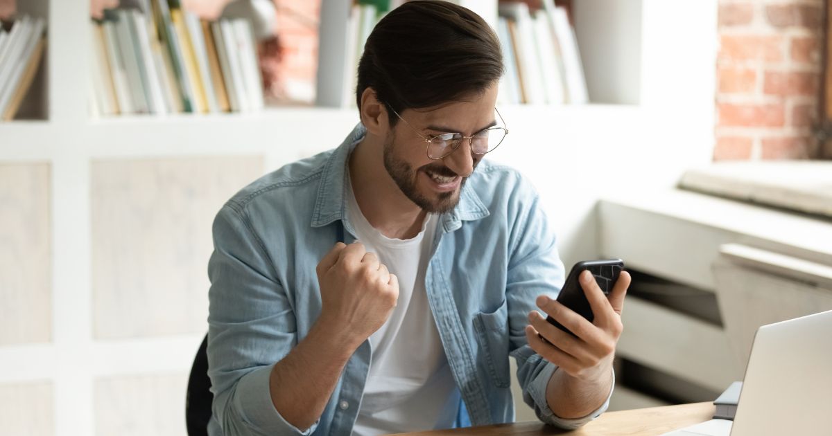 Professional man at his desk celebrates good news he sees on his cell phone