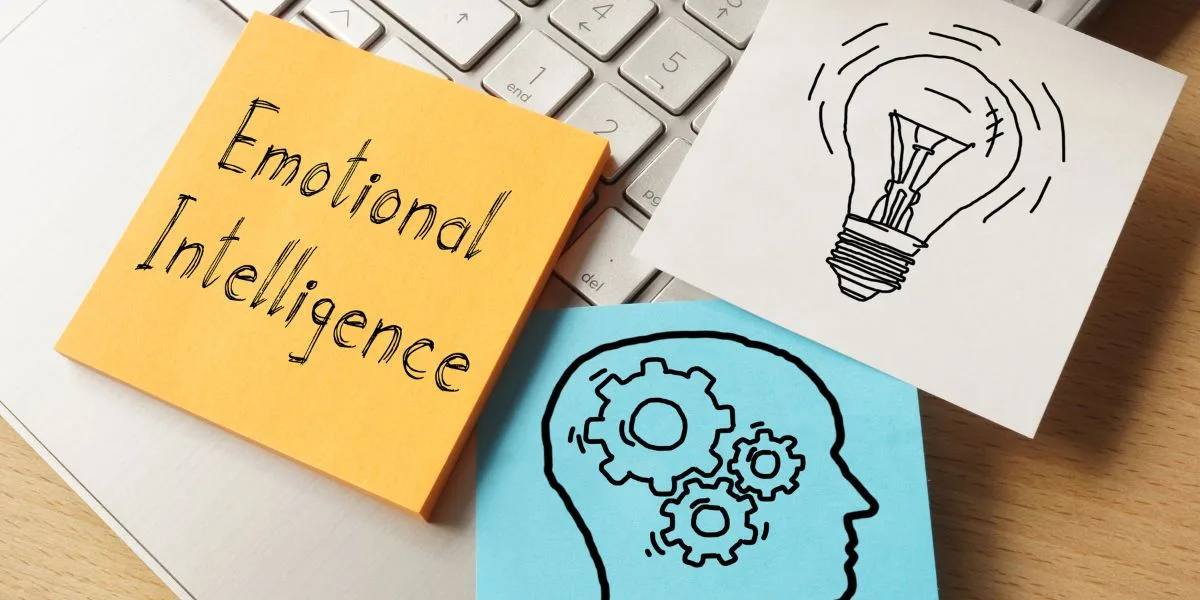Close up of a keyboard with three images and notes across the top. One says "Emotional Intelligence,' one is a head with gears, and one is a lightbulb.
