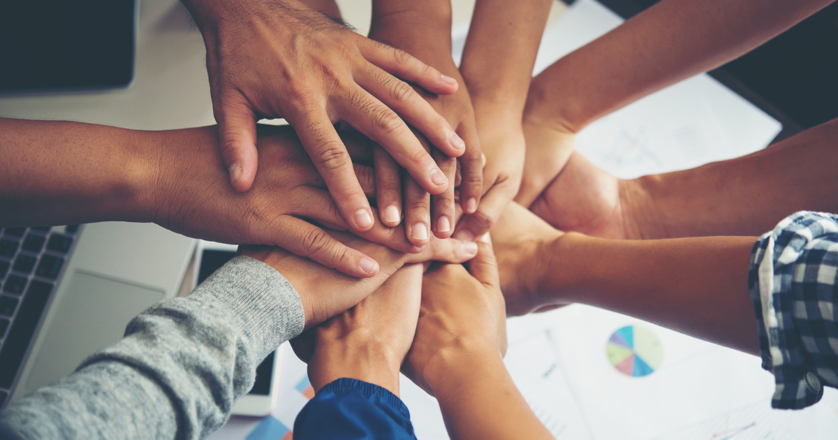 Group of diverse individuals, hands outstretched and placed on top of each other in team work.