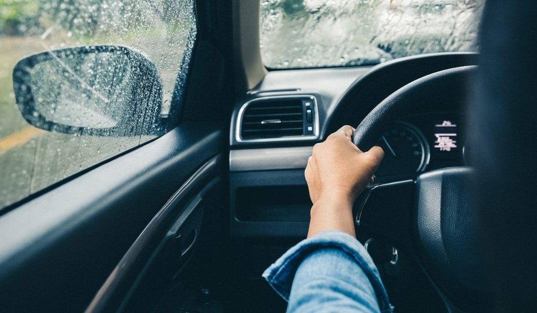 View of a driver, with hands on the steering wheel, driving in some rain