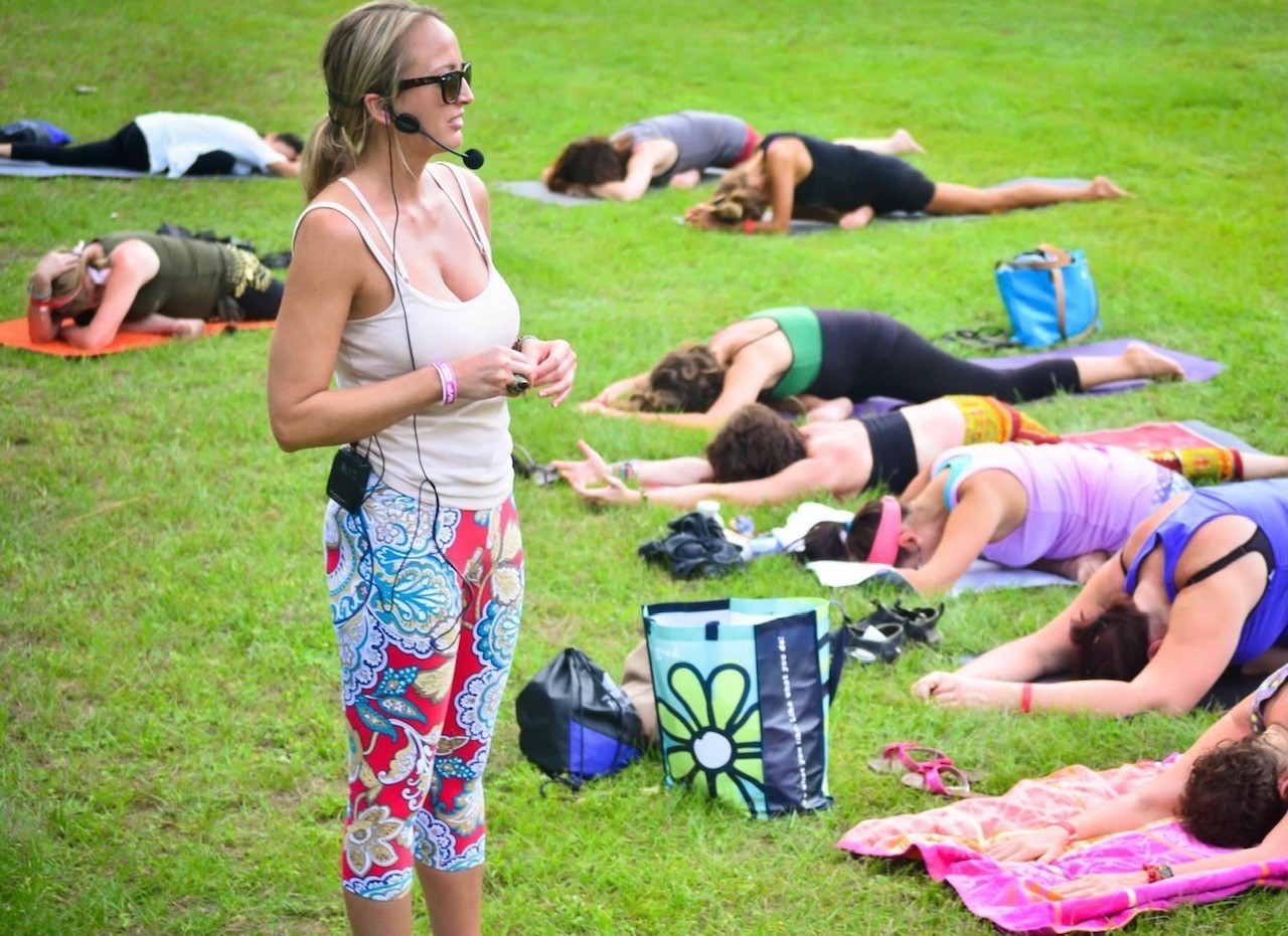 A woman teaching a yoga class on a grass field