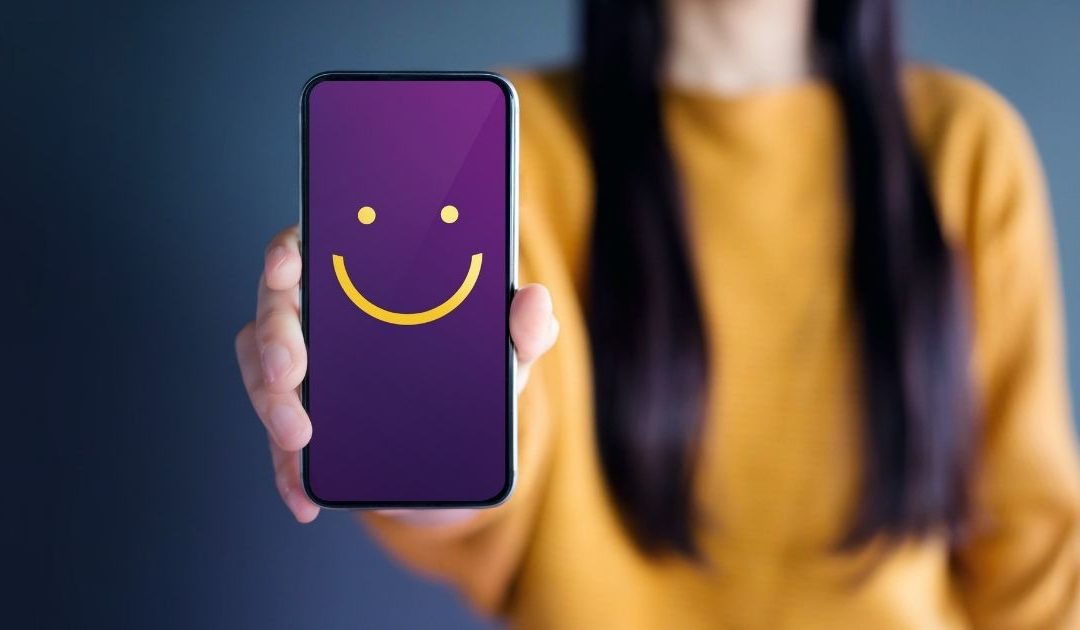Woman holding a phone out, with a big smiley face.