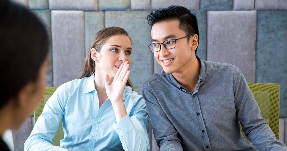 Young business woman telling Asian man a secret during a meeting