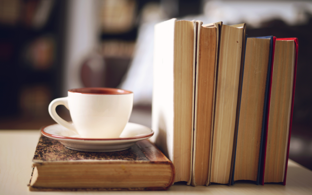 A stack of books and a cup of hot coffee on a table.