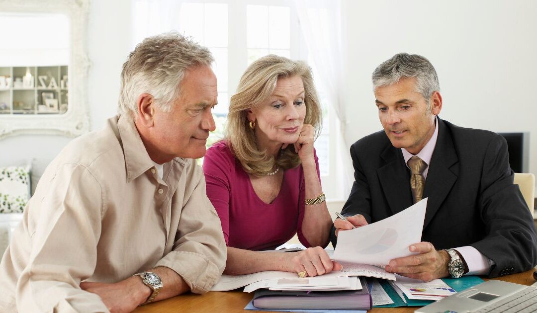 A middle aged couple sits at a table with a suited financial advisor, looking over their options.