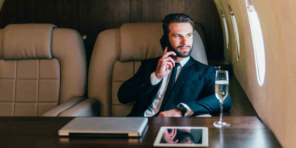 Affluent client sits at a desk on a private plane discussing finances with his advisor on the cell phone.