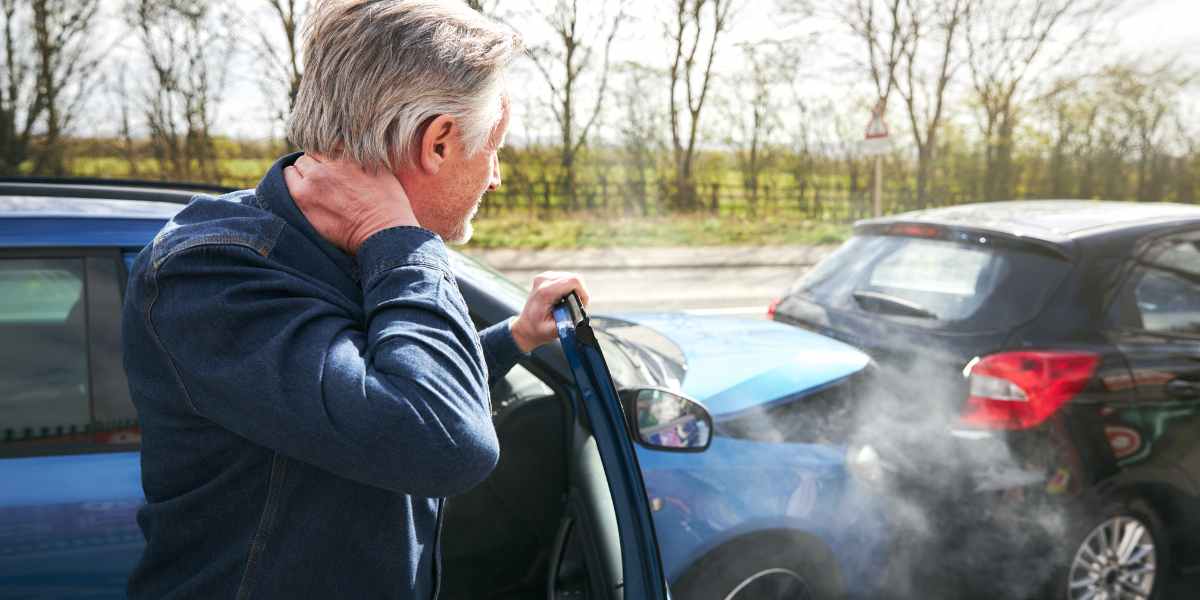 Mature man steps out of his car, holding his neck, following an auto accident.