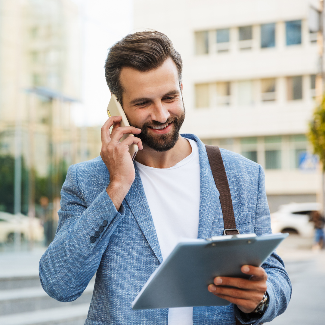 Professional man with a phone to his ear, standing outside, reviewing his tablet. 