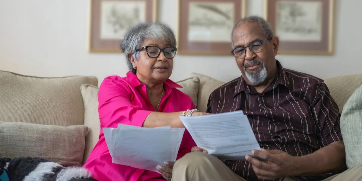 Happy couple sits on the couch, reviewing paperwork in front of them with their Medicare plans