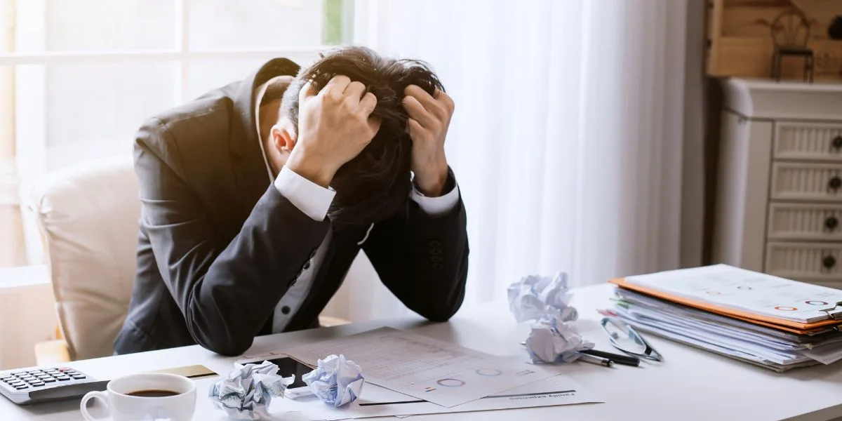 Frustrated financial advisor bends over his desk and grips his hair.