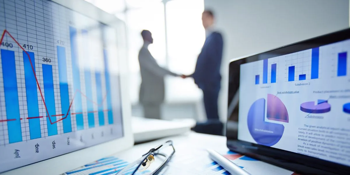 Medical professional and a marketing professional shake hands in the distance, with computers, graphs, and metrics sit in front.