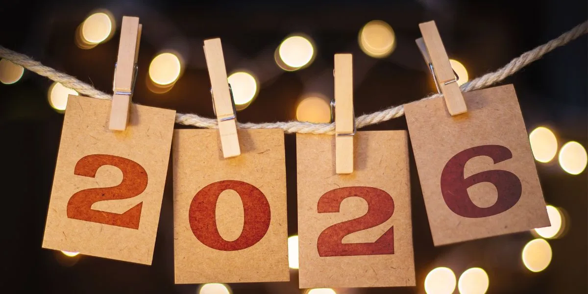 Notes with 2026 hang from a string by clothespins, with lights behind.