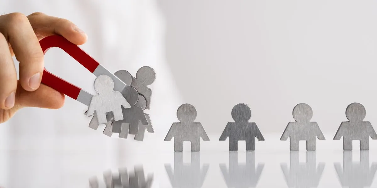 Hand holding a magnet draws metal human figures towards it