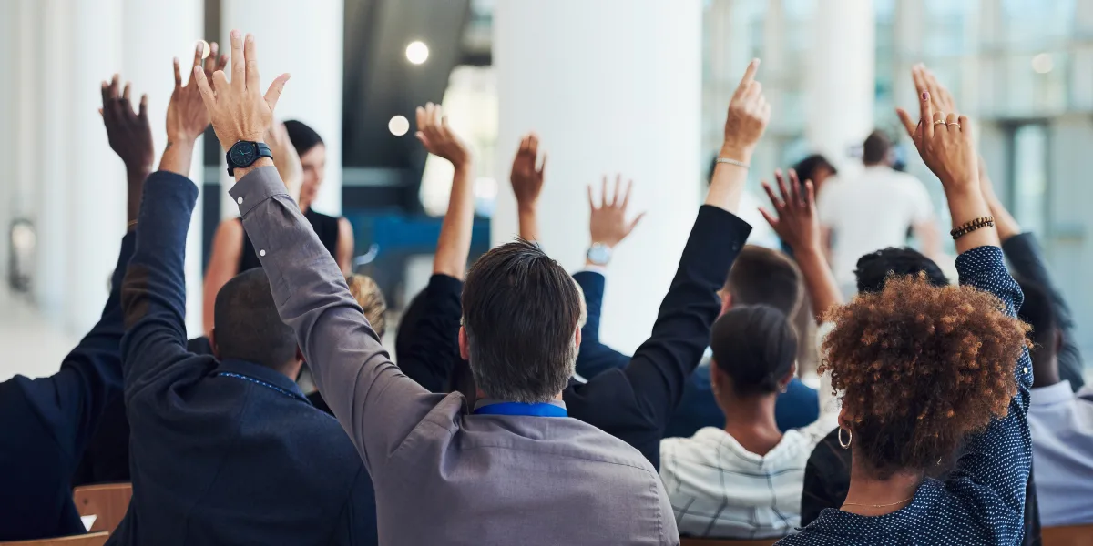 Seminar marketing audience raises hands to question financial advisor
