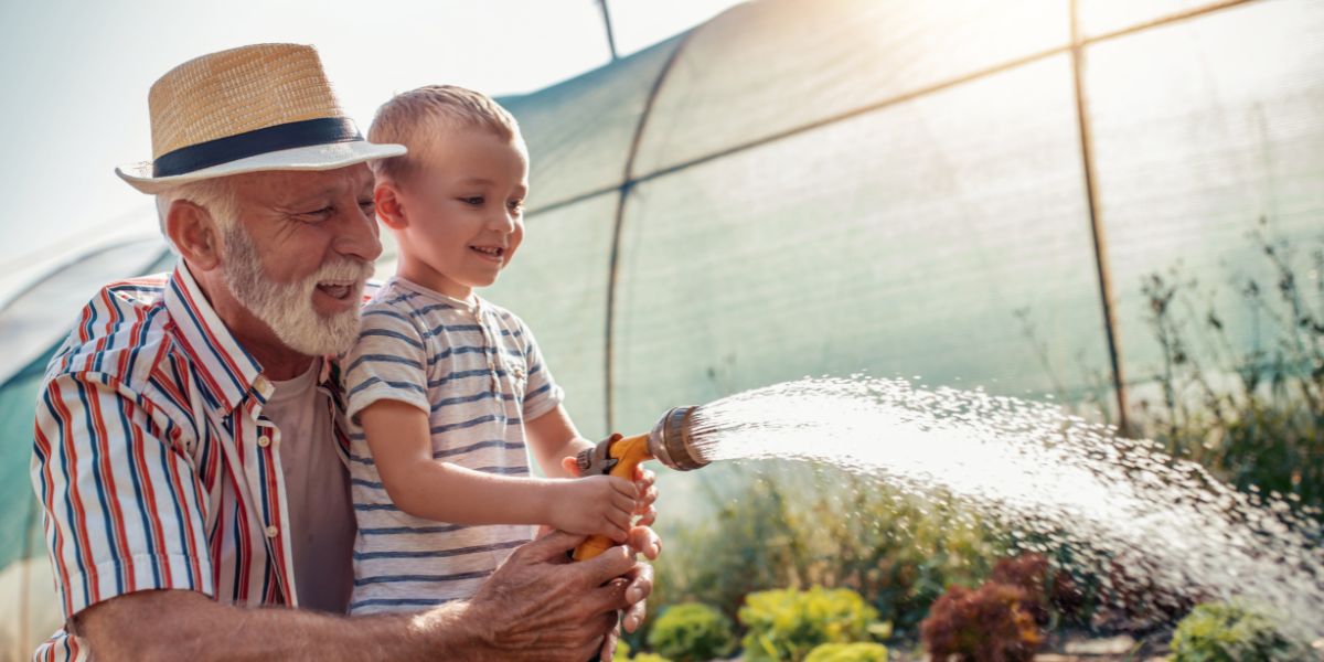Grandfather helping his grandson water the plants outside.